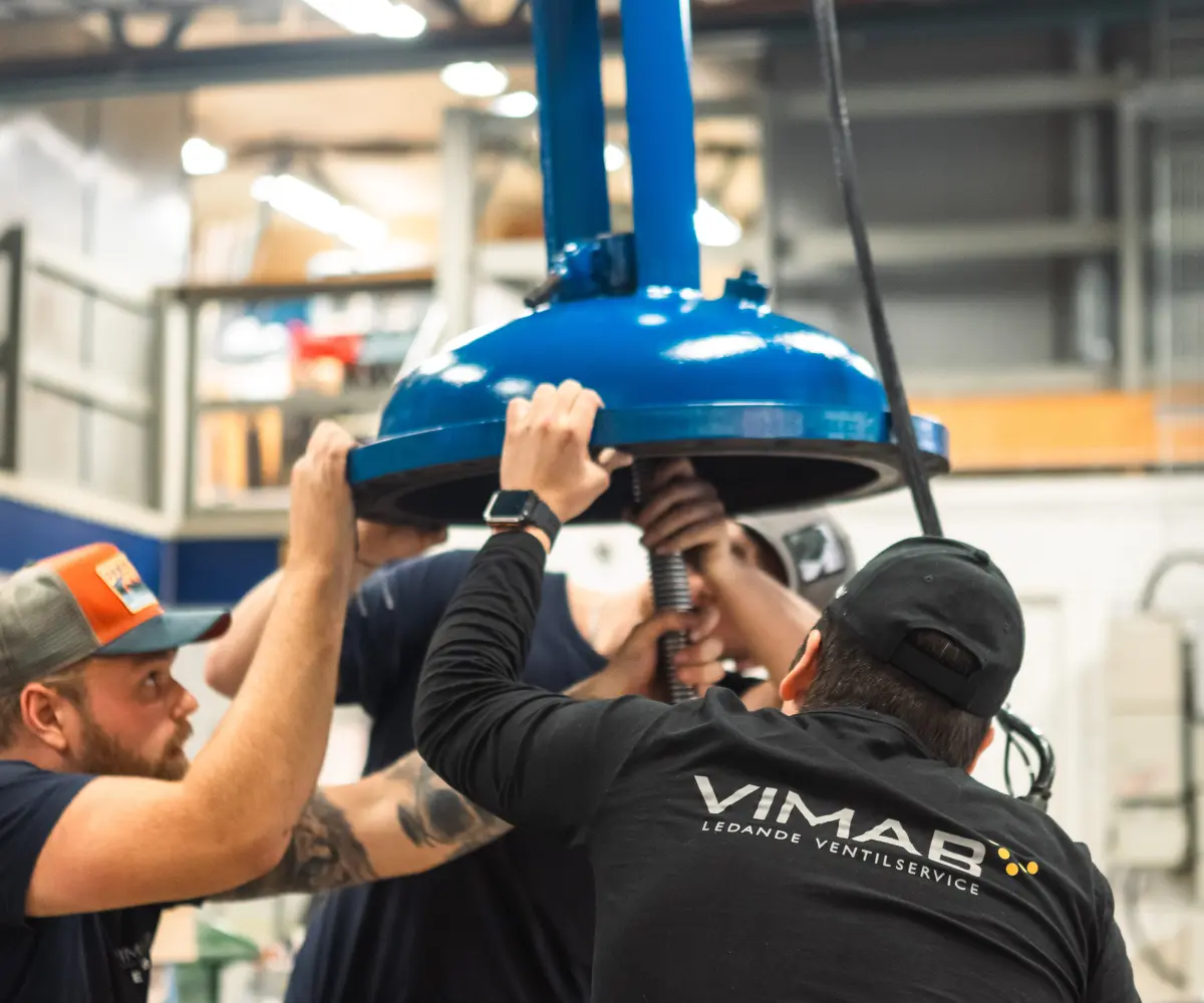 VIMAB-tekniker monterar stor blå industriventil i verkstad – tre ventiltekniker arbetar tillsammans